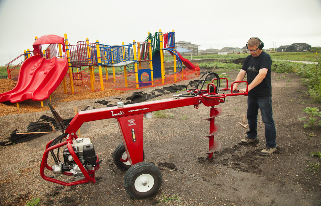 Towable earth auger used to drill a hole in a park